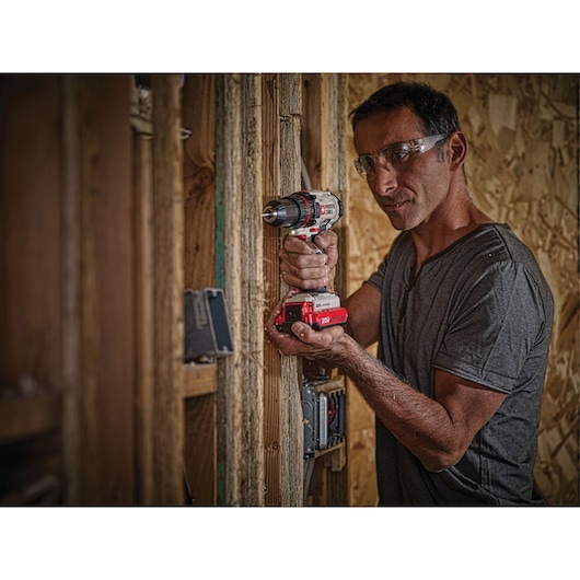 A person using a PORTER-CABLE cordless drill to drill into a wooden stud in a construction setting. The individual’s face is blurred for privacy.