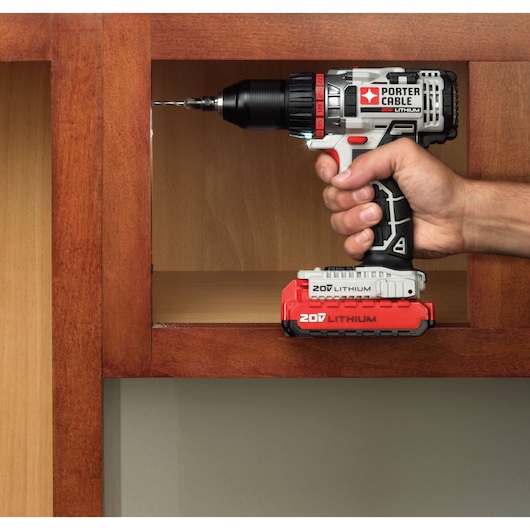 A person uses a PORTER-CABLE cordless drill with a 20V lithium battery to drill a hole in a wooden cabinet.