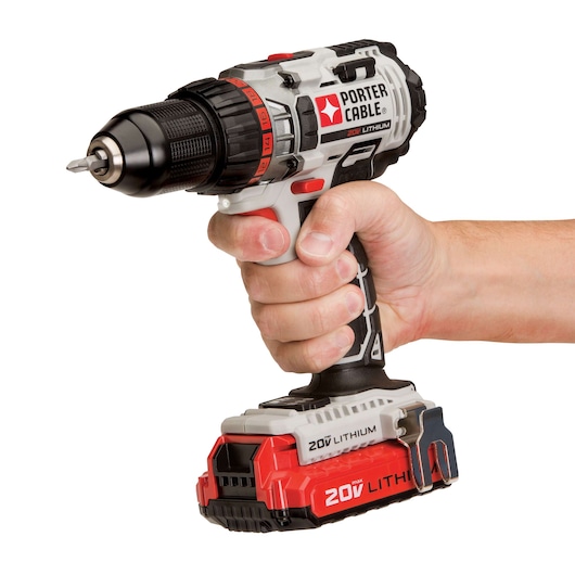 A hand holds a PORTER-CABLE cordless power drill with a 20V lithium battery. The drill is gray, black, and red, and features a metal clip on the battery pack.