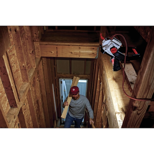 A PORTER-CABLE tool, likely a circular saw, is placed on a wooden beam inside an unfinished staircase area. The scene shows wooden framing and a person carrying lumber up the stairs.