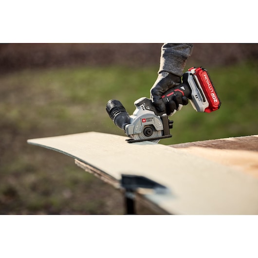 A close-up of a PORTER-CABLE cordless circular saw being used to cut through a piece of wood. The tool is held with a gloved hand and features a 20V lithium battery.