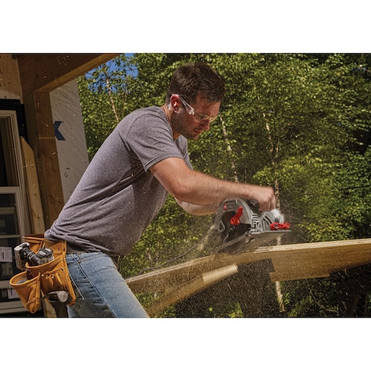 A person using a PORTER-CABLE circular saw, SKU PCE310, to cut wood outdoors. Sawdust is visible in the air, and the person has a tool belt with various tools attached.