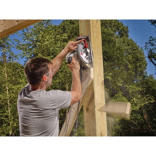 A person using a PORTER-CABLE circular saw to cut a piece of wood outdoors. The sawdust is visible in the air and a freshly cut piece of wood is falling away. The individual’s face is blurred for privacy.