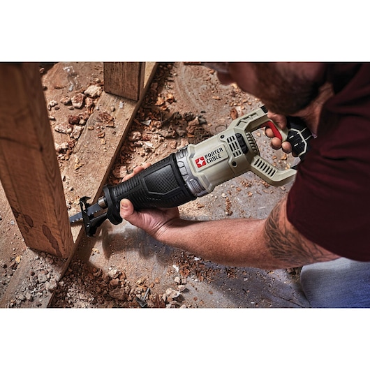A person uses a PORTER-CABLE reciprocating saw (model PCE360) to cut a wooden beam at a construction site. There are wood shavings and debris on the ground.
