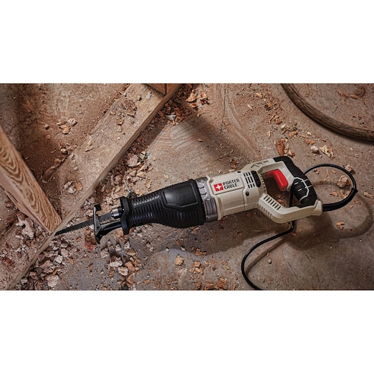 A PORTER-CABLE reciprocating saw model PCE360, placed on a dusty workshop floor next to wood debris and framing.