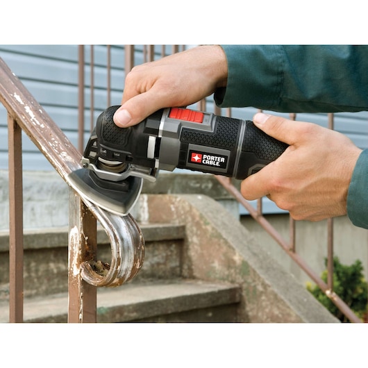 A person uses a PORTER-CABLE oscillating tool to sand or grind rust off a metal handrail outdoors, near steps.