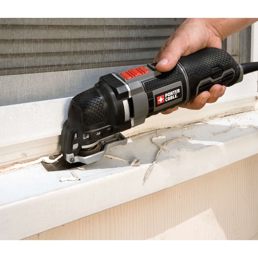 A person using a PORTER-CABLE oscillating multi-tool to cut or remove material from a window sill, with visible debris around the work area.