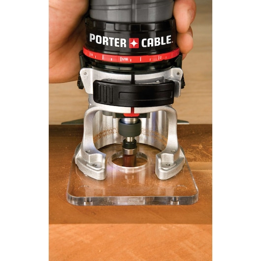 A close-up view of a PORTER-CABLE branded wood router being used on a piece of wood, showing the tool's base and cutting bit in operation.