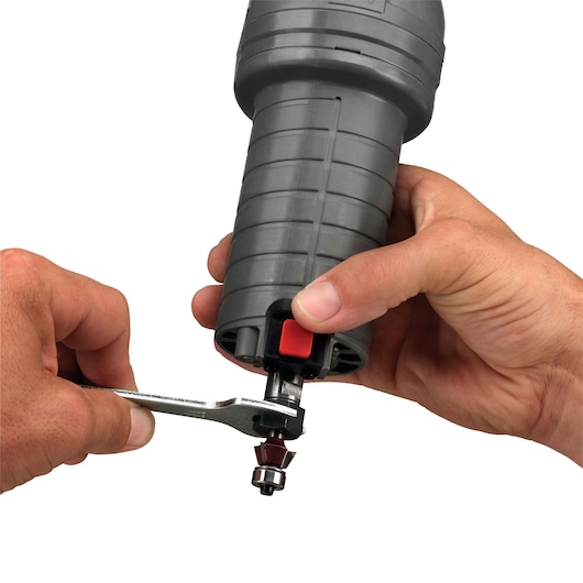 Close-up of hands adjusting the router bit on a PORTER-CABLE PCE6430 compact router tool using a wrench. The tool has a grey, ribbed body and a red button near the base.