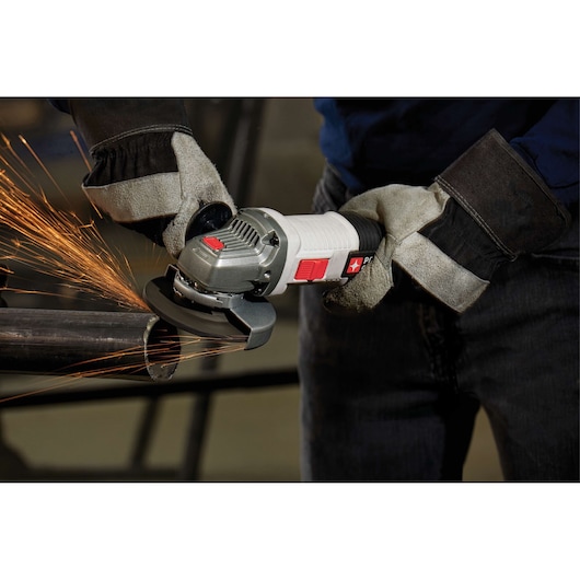 A person wearing protective gloves is using a PORTER-CABLE angle grinder to cut a metal pipe, producing sparks.