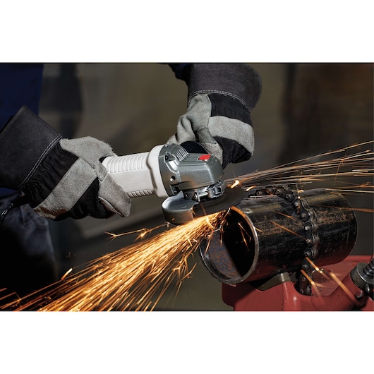 A person wearing protective gloves operates an angle grinder, cutting through a metal pipe and producing sparks.