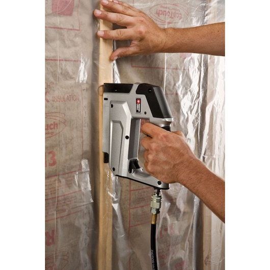 A person using a PORTER-CABLE pneumatic stapler (model TS056) to fasten plastic sheeting onto wall insulation.